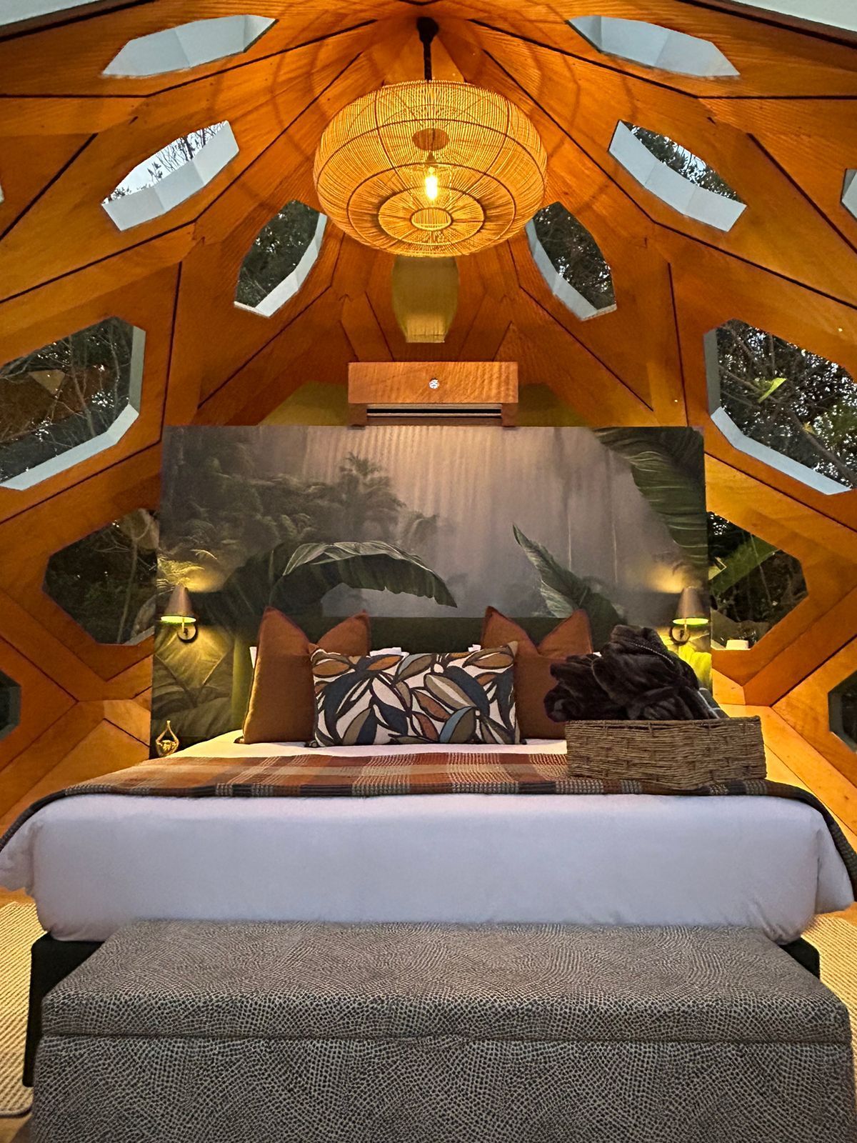Furnished GeoMod dome interior — timber honeycomb shell with a styled bed beneath the pendant light